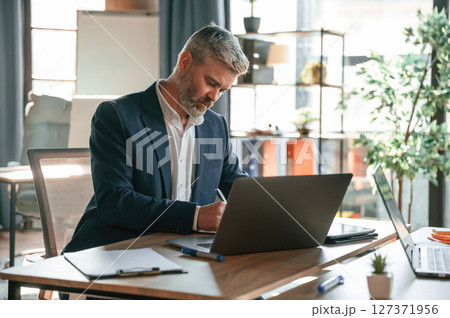 Using laptop. Senior businessman is working in the office Using laptop. Senior businessman is working in the office 127371956