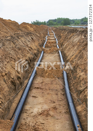 Water pipes for drinking water supply lie on the construction site. Preparation for earthworks for laying an underground pipeline. Modern water supply systems for a residential city. Water pipes for drinking water supply lie on the construction site. Preparation for earthworks for laying an underground pipeline. Modern water supply systems for a residential city. 127372354