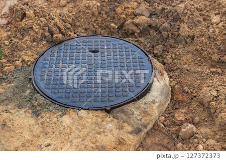 A cast-iron sewer manhole surrounded by a puddle of water at a construction site. Construction of sewer wells. A cast-iron sewer manhole surrounded by a puddle of water at a construction site. Construction of sewer wells. 127372373
