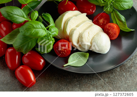 Mozzarella cheese with cherry tomatoes and basil on a stone table. 127372605