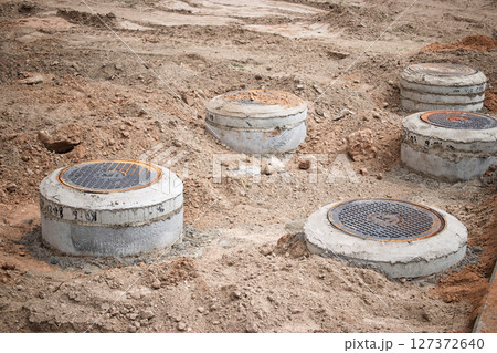 Construction site with several newly installed manhole covers surrounded by exposed soil 127372640
