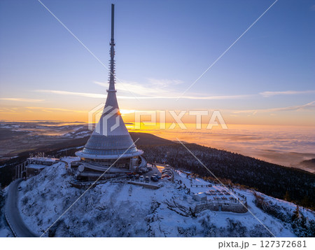Snow blankets Jested Mountain as the sun rises, casting a warm glow over the landscape. The iconic tower stands tall against the serene winter sky, creating a breathtaking view. Snow blankets Jested Mountain as the sun rises, casting a warm glow over the landscape. The iconic tower stands tall against the serene winter sky, creating a breathtaking view. 127372681