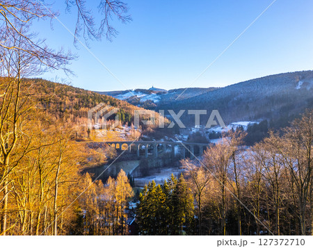 A picturesque railway stone bridge spans the valley in Novina, Krystofovo udoli, with the Jested Mountain looming in the background during a serene winter sunset, showcasing nature's beauty. A picturesque railway stone bridge spans the valley in Novina, Krystofovo udoli, with the Jested Mountain looming in the background during a serene winter sunset, showcasing nature's beauty. 127372710