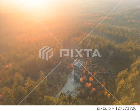 The Cisarsky Kamen wooden lookout tower stands tall among vibrant autumn trees, bathed in the warm glow of sunset, near Liberec, inviting viewers to enjoy the tranquil beauty of nature. The Cisarsky Kamen wooden lookout tower stands tall among vibrant autumn trees, bathed in the warm glow of sunset, near Liberec, inviting viewers to enjoy the tranquil beauty of nature. 127372726