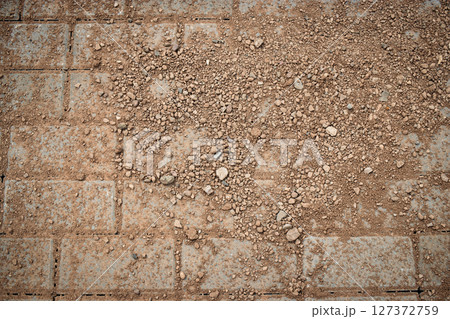 Ground surface with dirt and pebbles covering stone tiles in an outdoor setting during daylight 127372759