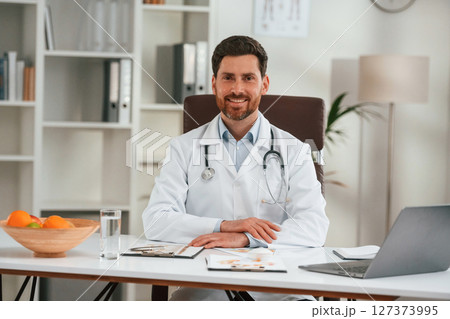 By the table with laptop. Doctor in formal clothes is working in the cabinet 127373995
