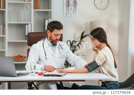 Measuring blood pressure. With woman. Doctor in formal clothes is working in the cabinet 127374056