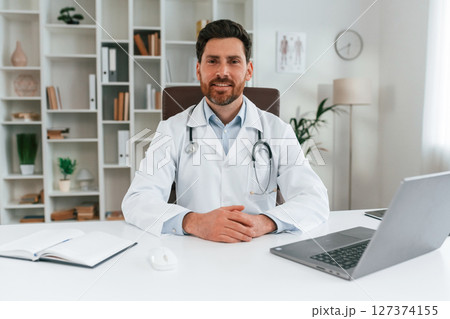 Sitting by a table. Doctor in formal clothes is working in the cabinet 127374155