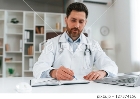 Sitting by a table. Doctor in formal clothes is working in the cabinet 127374156