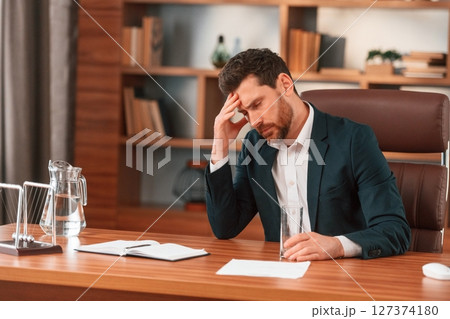Having headache, feeling bad. Businessman in formal clothes is working indoors Having headache, feeling bad. Businessman in formal clothes is working indoors 127374180