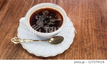 close up of a hot black coffee in a traditional porcelain cup with a tea spoon on a wooden table  with copy space 127374528