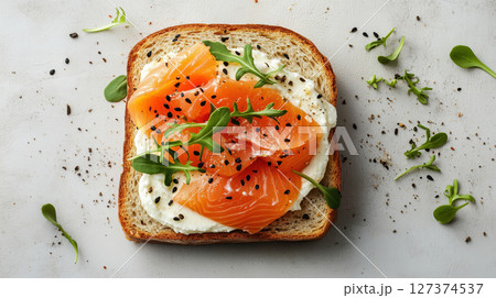 Open-faced sandwich with cream cheese, smoked salmon, arugula, and black sesame seeds on toast. Gourmet snack idea. Fresh and savory. 127374537