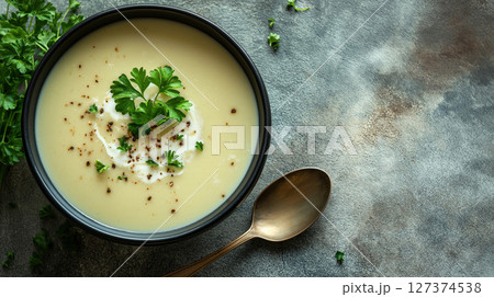 Creamy soup garnished with parsley, black pepper, and a swirl of cream in a black bowl. Warm and comforting meal. Rustic background. 127374538