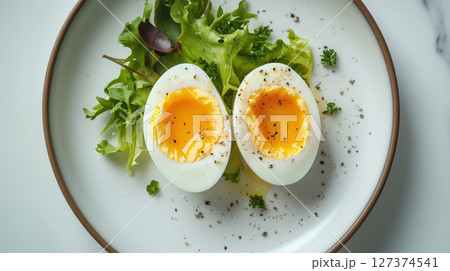 Soft-boiled egg halves served on fresh green lettuce leaves with ground pepper on a white plate. Simple and nutritious dish. Balanced meal. 127374541