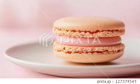 Single pink macaron with smooth filling placed on a white plate over a soft pink background. Elegant and delicate dessert. French classic. 127374543