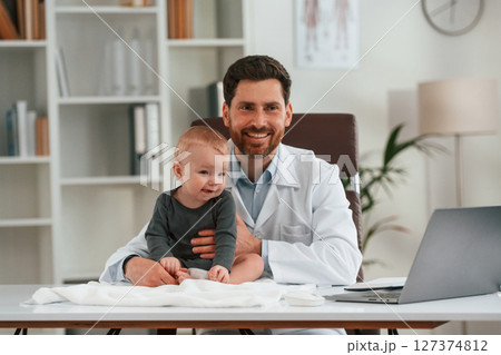 Friendly positive doctor with little baby is working in the cabinet 127374812