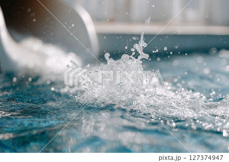 Water splash in a swimming pool with vibrant blue tiles and a water slide in the background 127374947