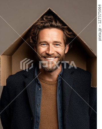 Confident man brings joy with a creative cardboard house setup while smiling 127375064