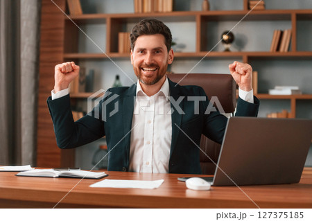Celebrating success. Businessman in formal clothes is working indoors Celebrating success. Businessman in formal clothes is working indoors 127375185