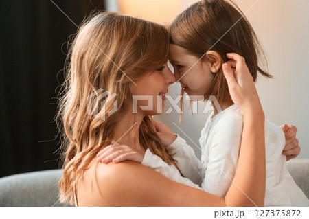 Side view, embracing each other. Mother with her little daughter is together in domestic room Side view, embracing each other. Mother with her little daughter is together in domestic room 127375872