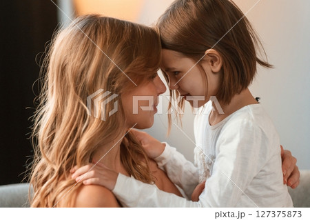 Side view, embracing each other. Mother with her little daughter is together in domestic room Side view, embracing each other. Mother with her little daughter is together in domestic room 127375873