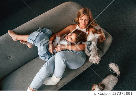 Positive emotions, relaxing on the sofa. Mother with her daughter and with two cute dogs is in domestic room 127375891