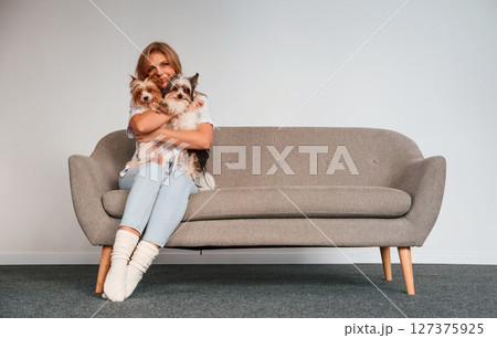 Conception of care and love. Woman is sitting on a sofa with two cute dogs Conception of care and love. Woman is sitting on a sofa with two cute dogs 127375925