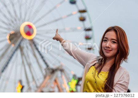 A joyful young woman pointing at a colorful ferris wheel, capturing the fun atmosphere of a carnival night. 127376012