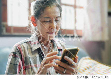 An elderly woman engages with her smartphone, highlighting technology's role in modern daily life. 127376016