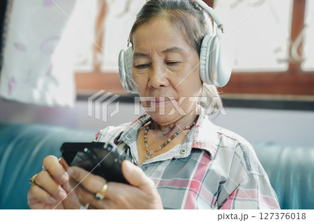 An elderly woman wears headphones while enjoying music on her smartphone, highlighting technology's impact on daily life. An elderly woman wears headphones while enjoying music on her smartphone, highlighting technology's impact on daily life. 127376018