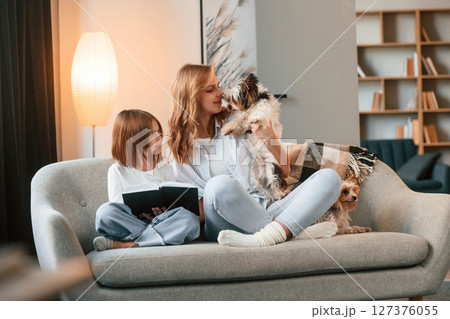 Reading the book. Mother with her daughter and with two cute dogs is in domestic room 127376055