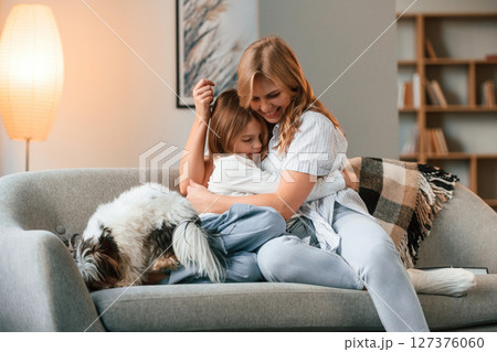 On the sofa. Mother with her daughter and with cute dog is in domestic room On the sofa. Mother with her daughter and with cute dog is in domestic room 127376060