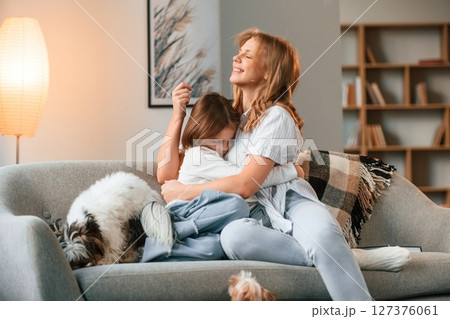 On the sofa. Mother with her daughter and with cute dog is in domestic room On the sofa. Mother with her daughter and with cute dog is in domestic room 127376061