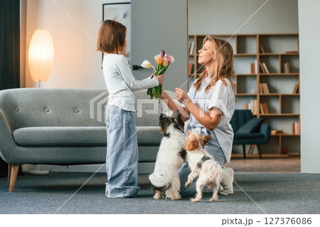 With flowers. Mother with her daughter and with two cute dogs is in domestic room 127376086