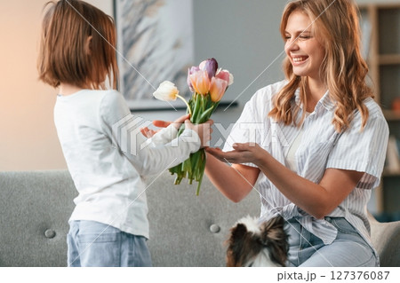 Happy mother's day, giving flowers. Woman with her little daughter is together in domestic room 127376087
