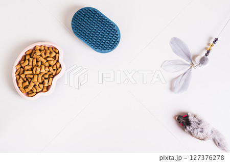 Bowl with dry cat food granules, brush and toys on light background top view Bowl with dry cat food granules, brush and toys on light background top view 127376278