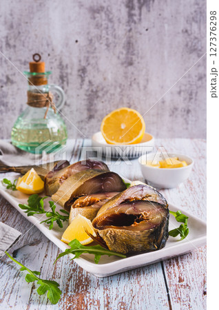 Cold smoked mackerel pieces, lemon and arugula on a plate on the table vertical view Cold smoked mackerel pieces, lemon and arugula on a plate on the table vertical view 127376298