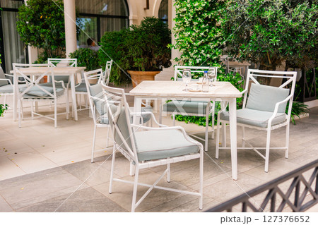 Elegant outdoor cafe terrace with white furniture and lush greenery. Relaxation, summer lifestyle, and modern hospitality. 127376652