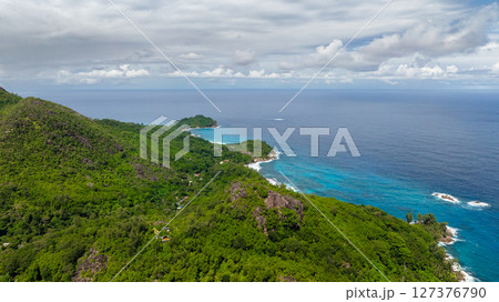 Aerial view of a lush green coastline with hills meeting the blue ocean under a cloudy sky. Seychelles, Mahe. 127376790