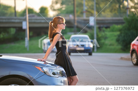 Young woman driver enjoying warm summer day standing beside her car on city street. Travelling and vacation concept Young woman driver enjoying warm summer day standing beside her car on city street. Travelling and vacation concept 127376972