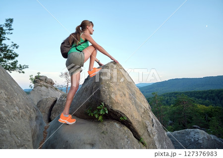 Young woman climbing alone on rocky mountain path. Female hiker enjoying difficult challenge on wilderness trail. Active way of life concept Young woman climbing alone on rocky mountain path. Female hiker enjoying difficult challenge on wilderness trail. Active way of life concept 127376983