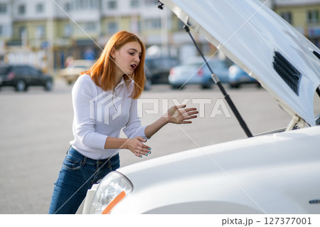 Young stressed woman driver standing near broked car with open hood. 127377001