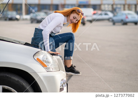 Young stressed woman driver near broken car with popped hood waiting for assistance. 127377002