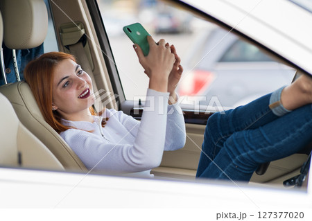 Young redhead woman driver taking selfies with her mobile phone sitting behind the wheel of the car in rush hour traffic jam. 127377020