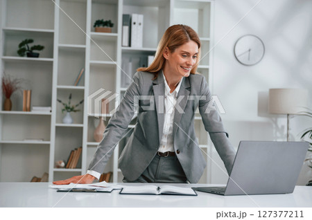 Standing by the table. Woman in business formal clothes is working in office Standing by the table. Woman in business formal clothes is working in office 127377211