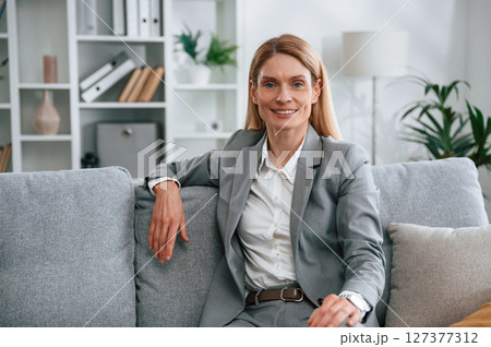 Front view. Woman in formal clothes is at home, sitting on the sofa Front view. Woman in formal clothes is at home, sitting on the sofa 127377312