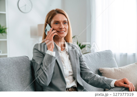 Having a call. Woman in formal clothes is at home, sitting on the sofa Having a call. Woman in formal clothes is at home, sitting on the sofa 127377319
