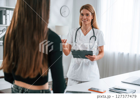 Standing, giving advice, holding notepad. Young woman at a nutritionist's appointment. Medical care Standing, giving advice, holding notepad. Young woman at a nutritionist's appointment. Medical care 127377479