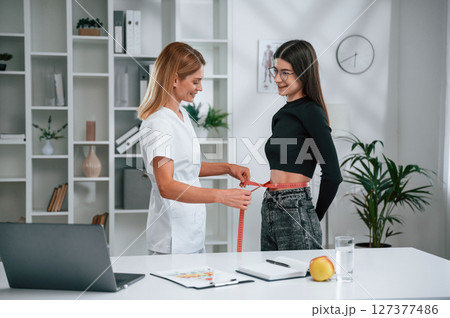 Conception of diet, gain weight, measuring the waist. Young woman at a nutritionist's appointment. Medical care 127377486