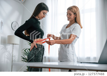 Measuring the waist. Young woman at a nutritionist's appointment. Medical care Measuring the waist. Young woman at a nutritionist's appointment. Medical care 127377488